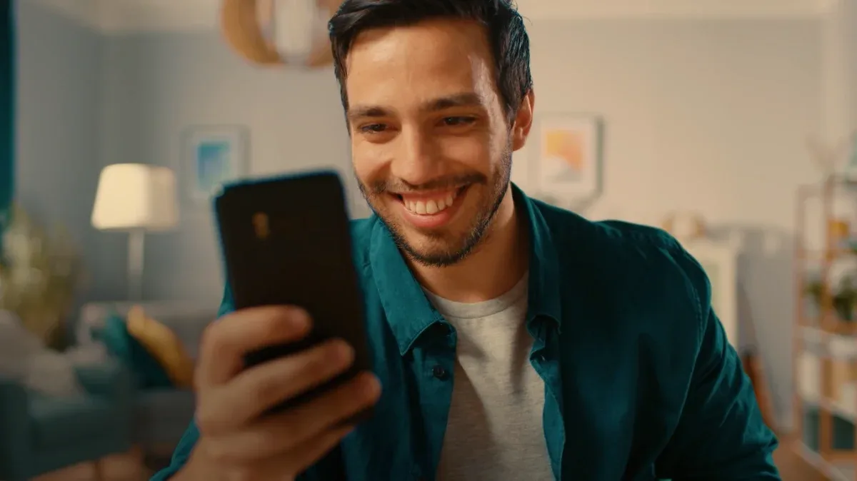 Homem sorri enquanto usa o celular na sala de casa