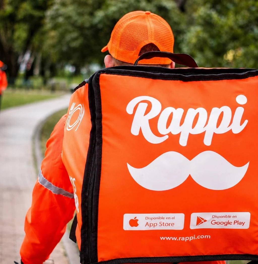 Delivery courier on a bicycle wearing a Rappi backpack, seen from behind